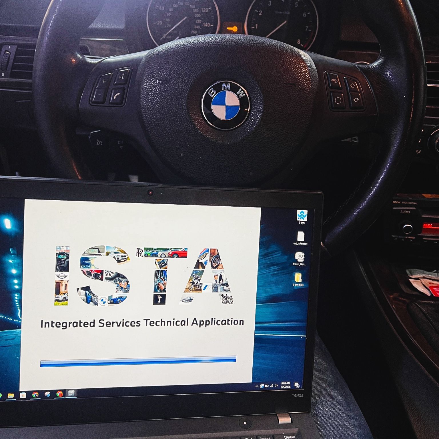 Laptop showing the BMW ISTA diagnostic software start screen, positioned in front of a BMW steering wheel